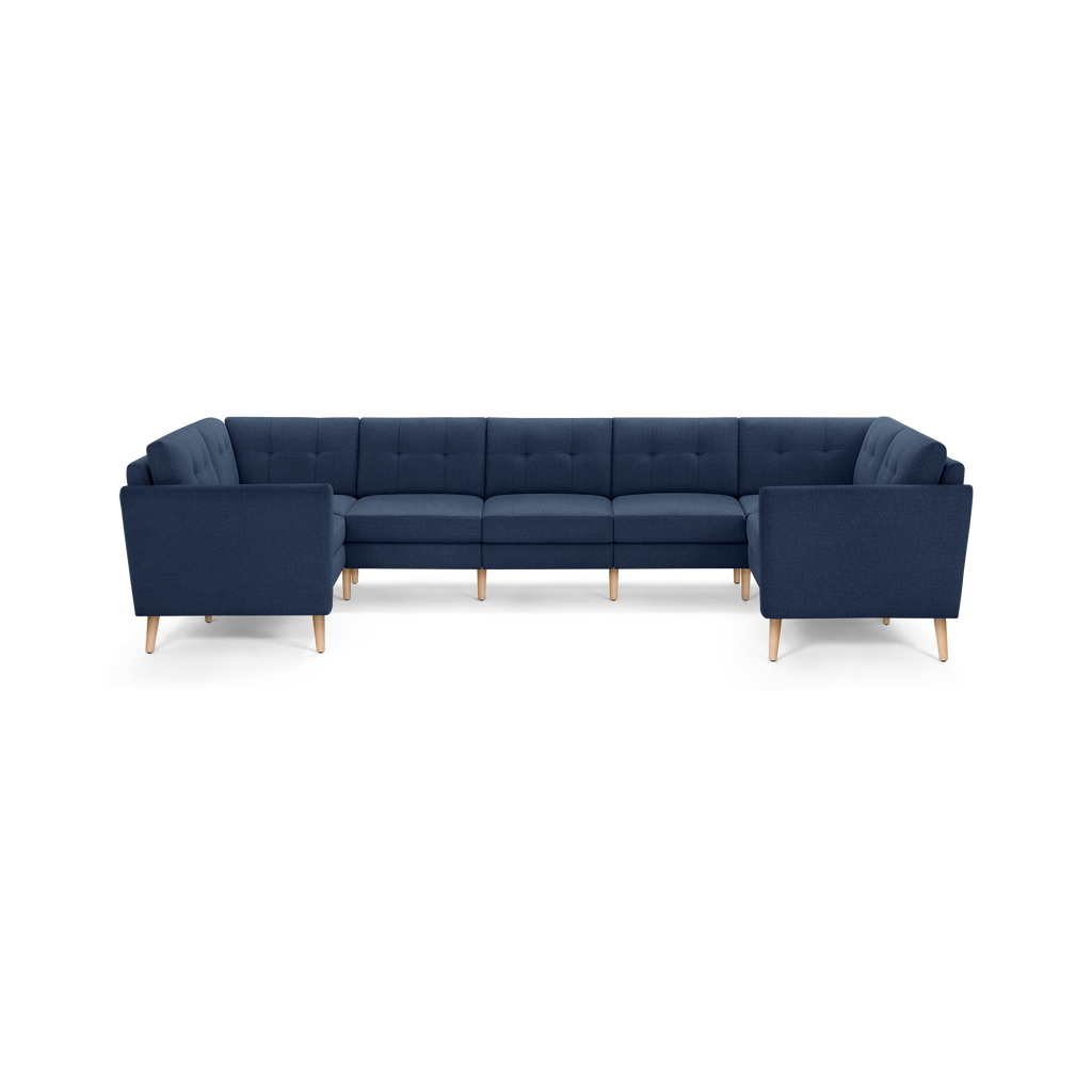 Large modern U-shaped sectional sofa in navy blue fabric with tufted back cushions and light wooden tapered legs.
