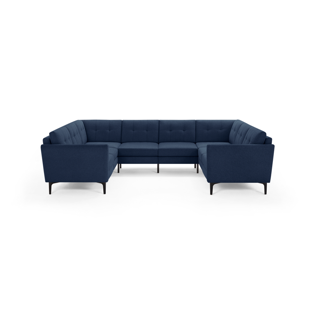 Large modern U-shaped sectional sofa upholstered in dark blue fabric with tufted back cushions and slim black legs.