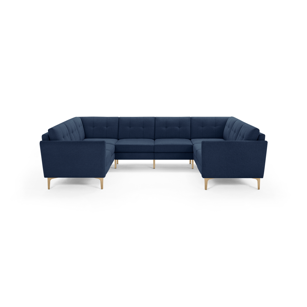 Large navy blue sectional sofa with tufted back cushions and light wooden legs, shown against a black background.