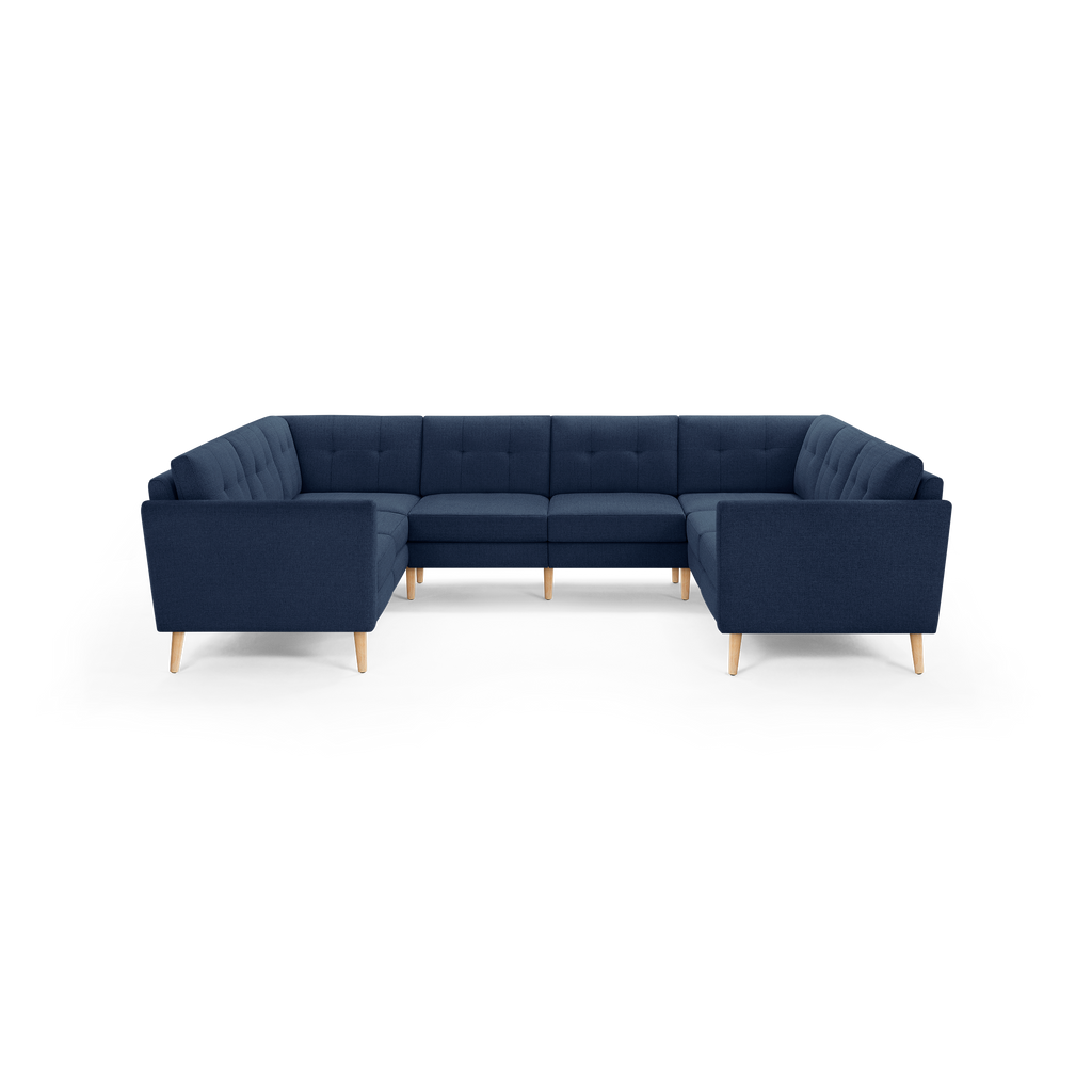Large U-shaped sectional sofa with deep blue fabric upholstery, tufted back cushions, and light wooden tapered legs.