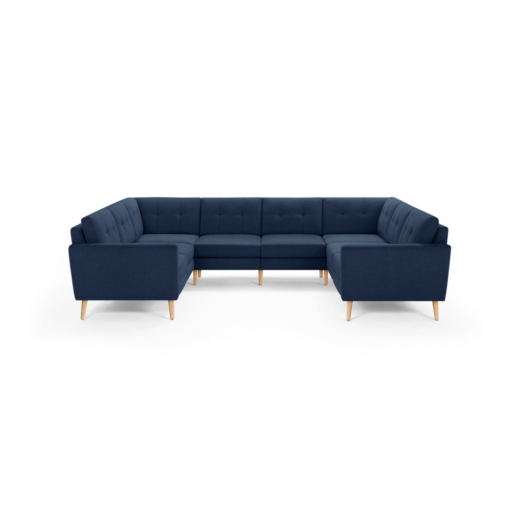 Large navy blue U-shaped sectional sofa with tufted cushions and light wooden legs, modern Scandinavian-style design.