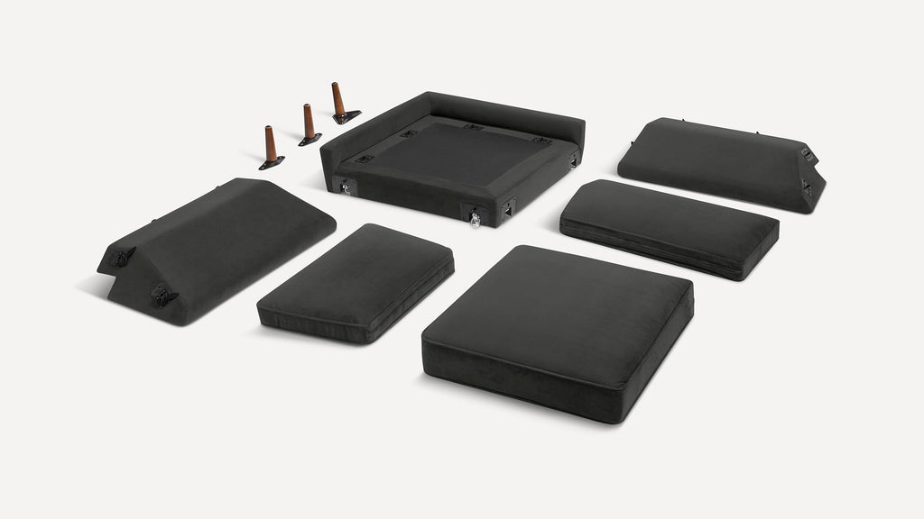 Black modular sofa pieces and wooden legs displayed separately on a white background for assembly.