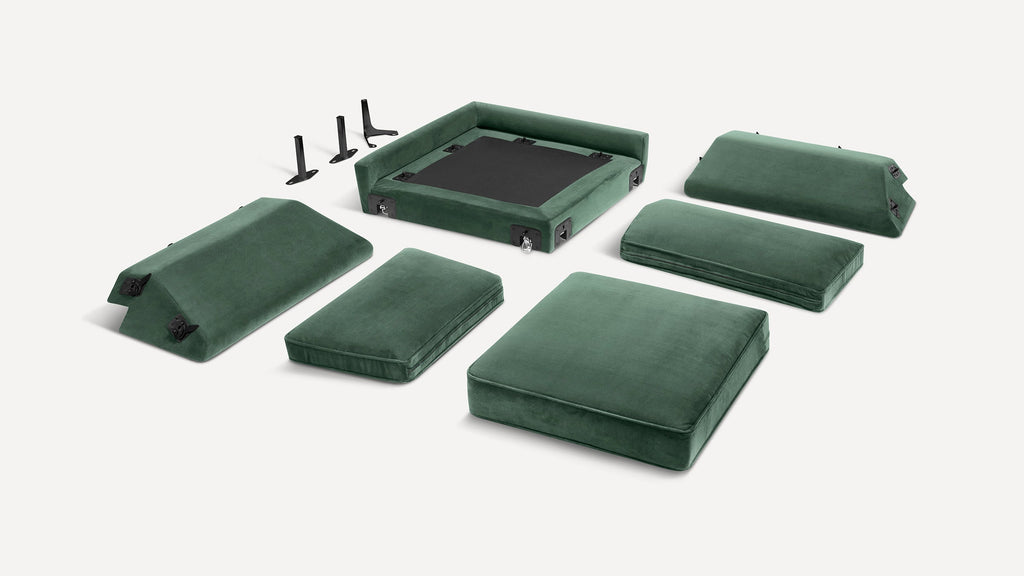 Disassembled green velvet sofa cushions and frame parts, including seating, backrests, and black metal support legs on a white background.