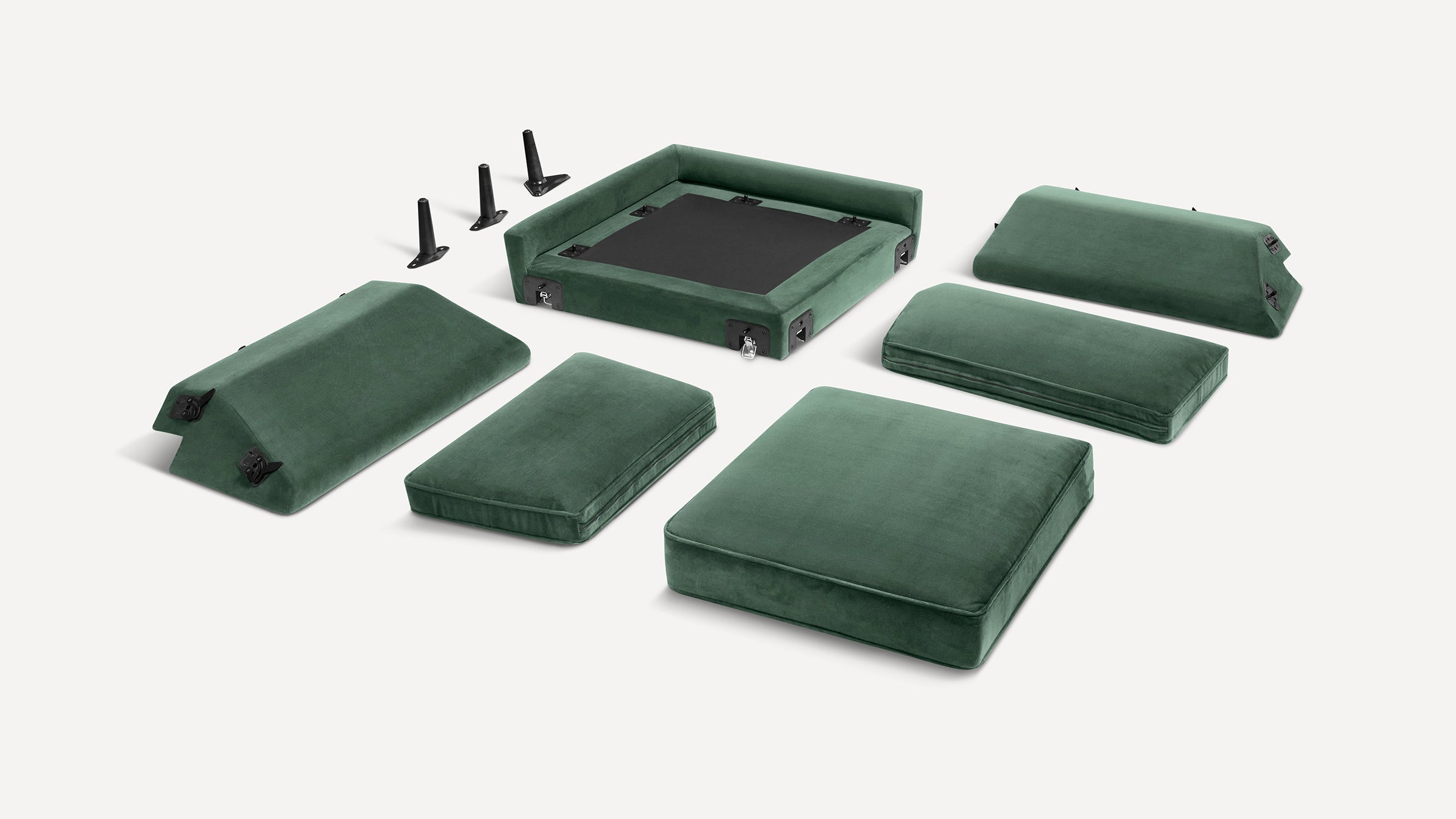 Disassembled green velvet modular sofa with cushions, backrests, base, and detachable black legs on a white background.