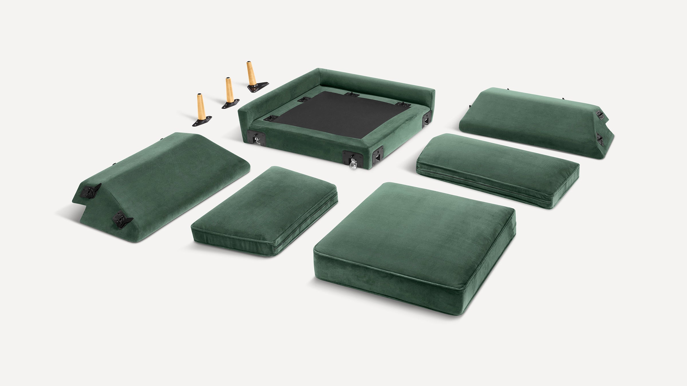 Disassembled green velvet modular sofa with cushions, backrests, and wooden legs laid out on a white background.