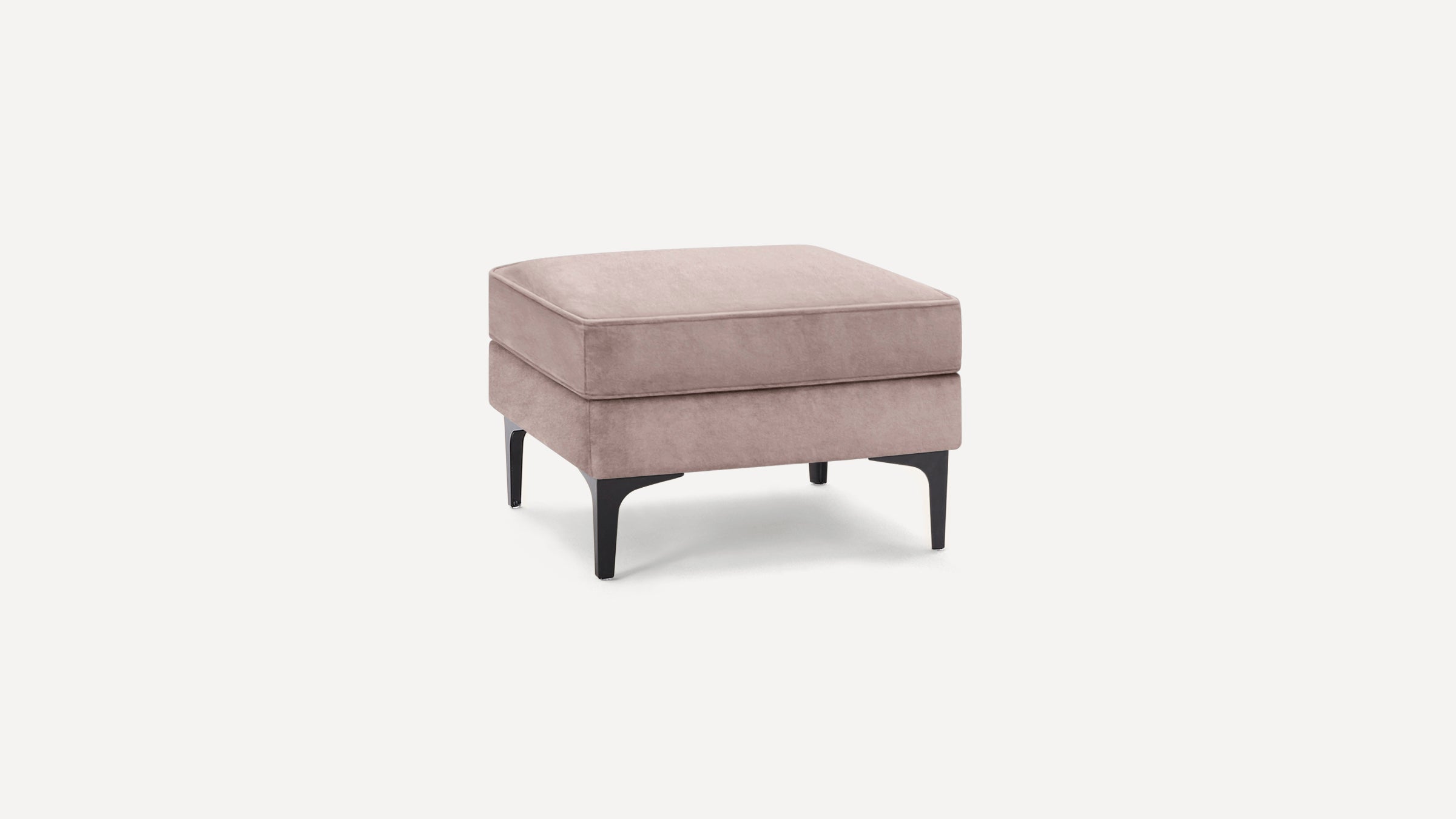 Square modern ottoman with soft pink velvet upholstery and sleek black angled legs on white background.