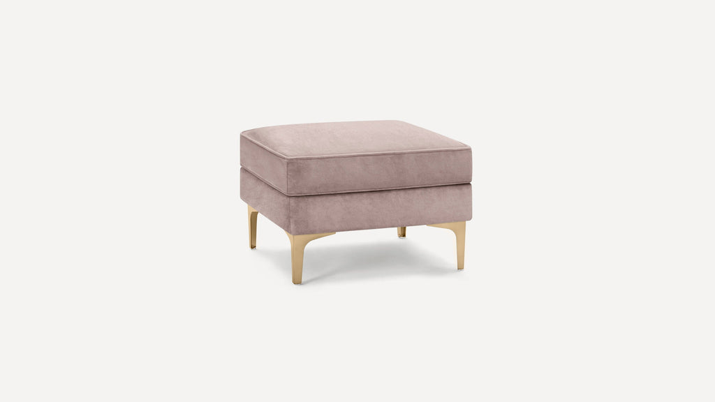 Square blush pink velvet ottoman with gold metal legs, featuring a cushioned top and modern design.