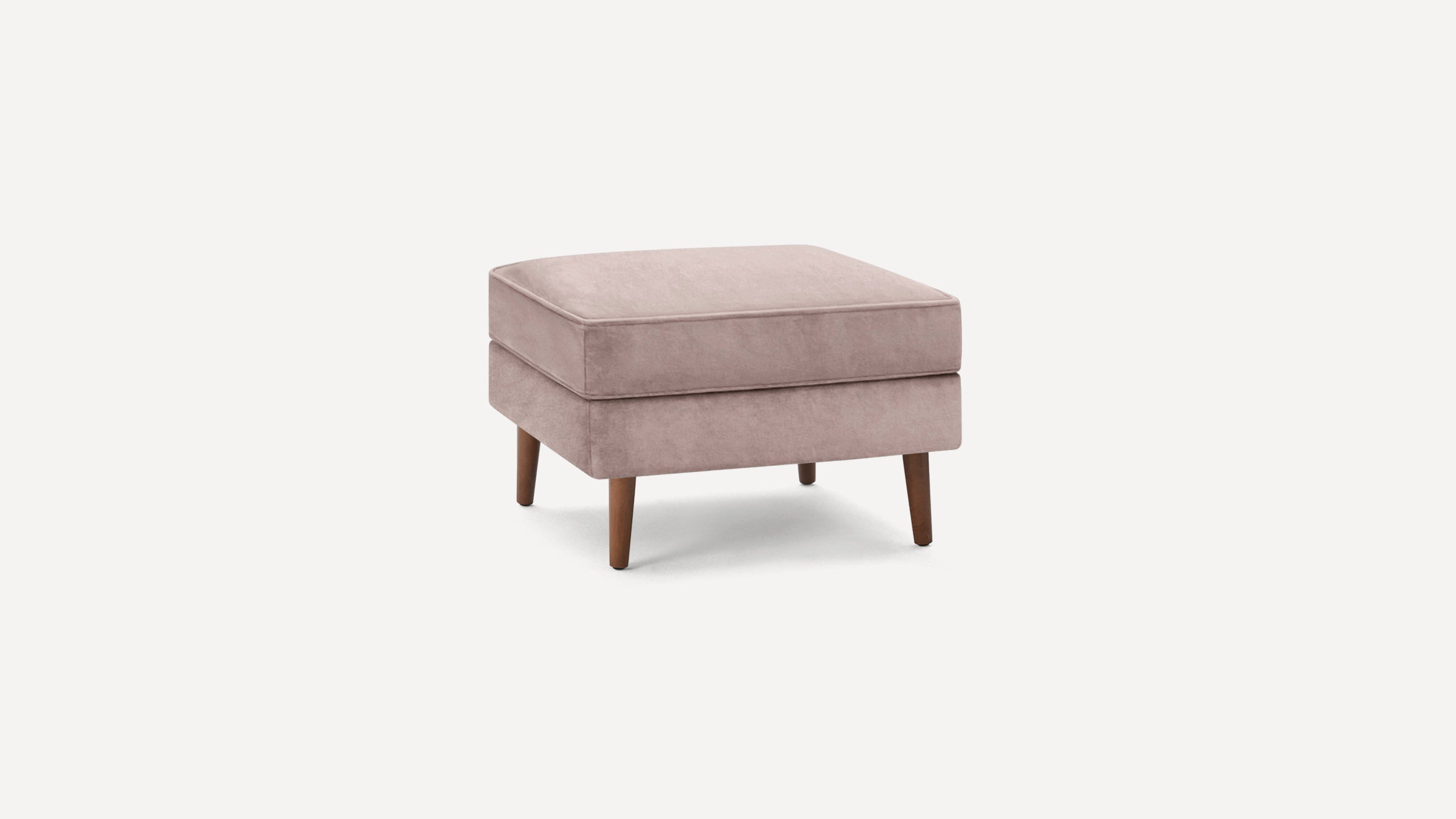 Square ottoman with plush pink velvet cushion and four wooden tapered legs on white background.