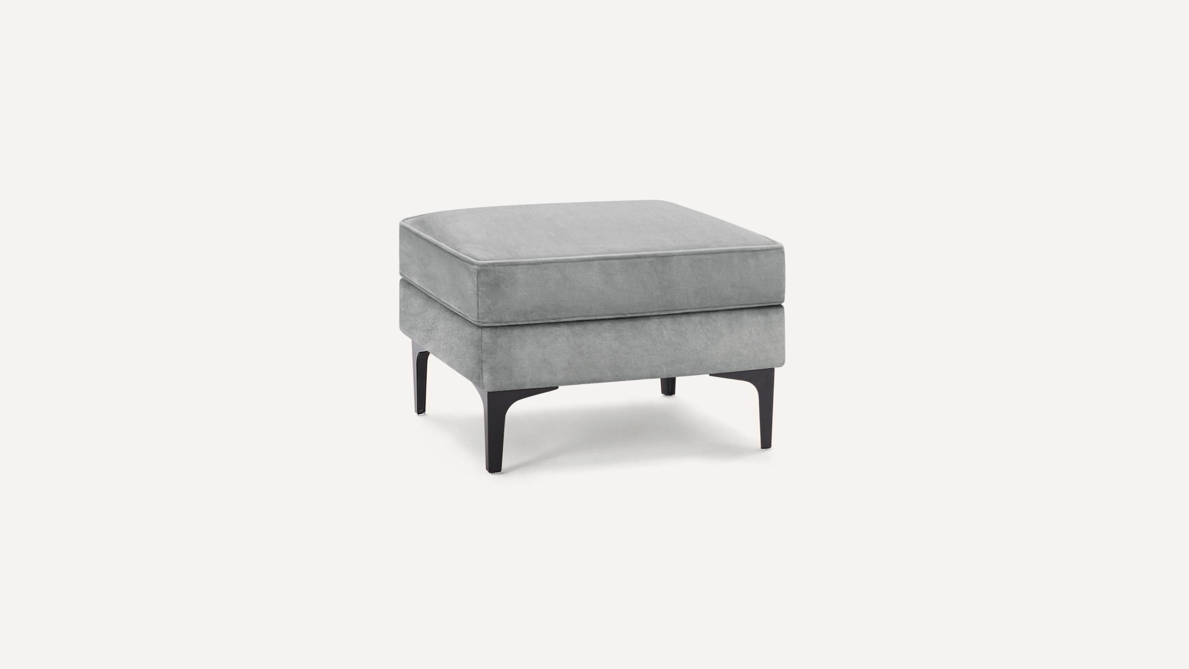 Square gray velvet ottoman with black tapered legs on a white background.