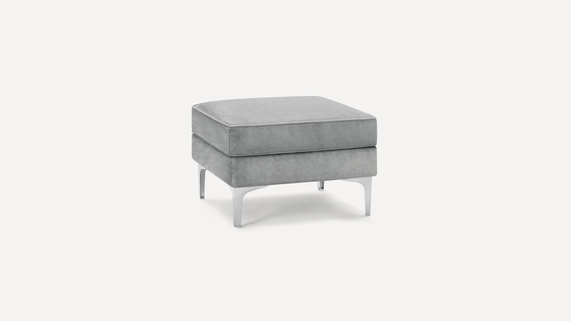 Modern square gray velvet ottoman with cushioned top and sleek silver metal legs, isolated on white background.
