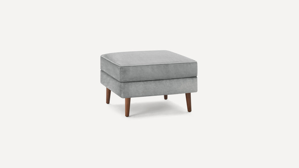 Square light gray upholstered ottoman with wooden tapered legs on a white background.
