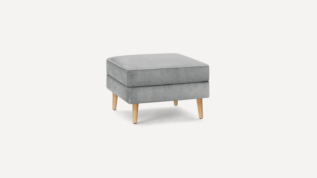 Square gray upholstered ottoman with soft cushion top and four light wooden legs on white background.
