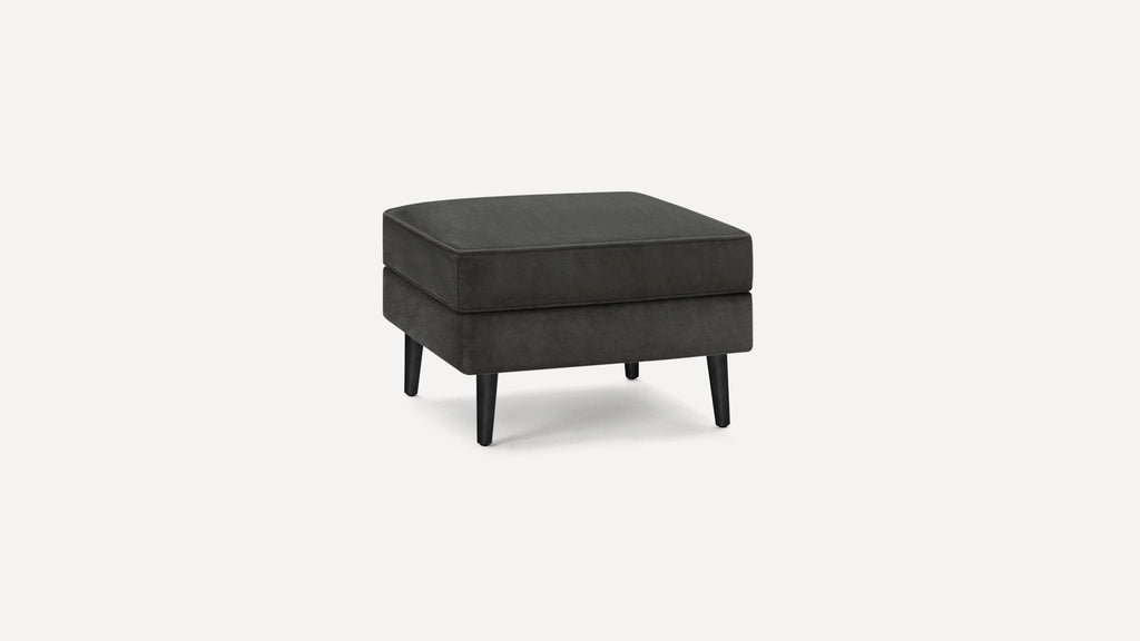 Dark gray upholstered square ottoman with cushioned top and four tapered black wooden legs on a white background.