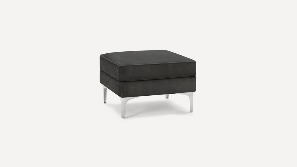 Square black upholstered ottoman with a cushioned top and sleek silver metal legs on a white background.
