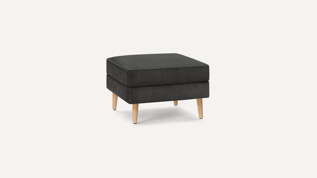 Modern dark gray square ottoman with soft cushion and light wooden tapered legs on white background.