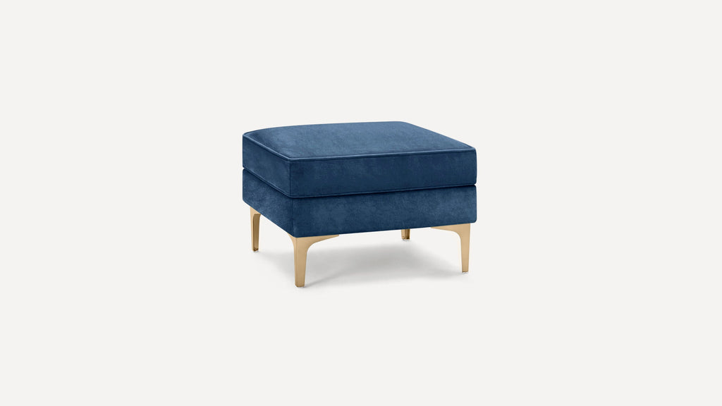 Square blue velvet ottoman with gold metal legs, featuring clean lines and modern design on a white background.