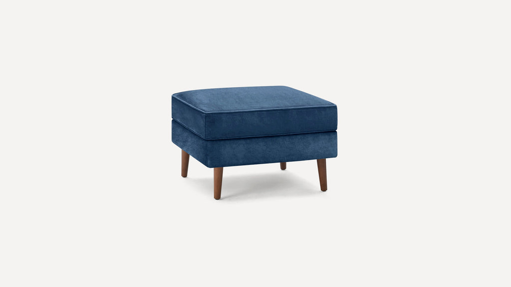 Square navy blue upholstered ottoman with tapered wooden legs on a light background.