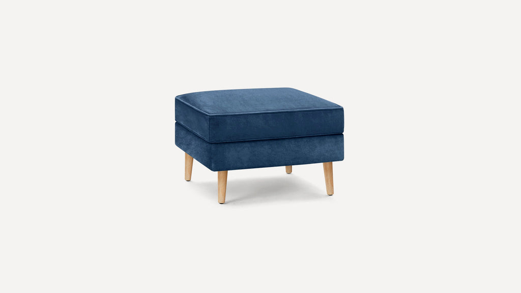 Square navy blue upholstered ottoman with wooden tapered legs, featuring a cushioned top and modern design.