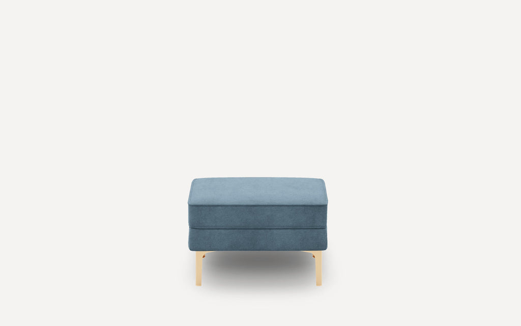 Rectangular blue upholstered ottoman with smooth fabric, gold-toned metal legs, and minimalist modern design on a white background.