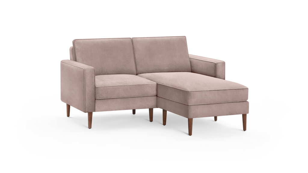 modern light pink velvet sectional sofa with wooden legs and matching ottoman, featuring a clean, minimalist design