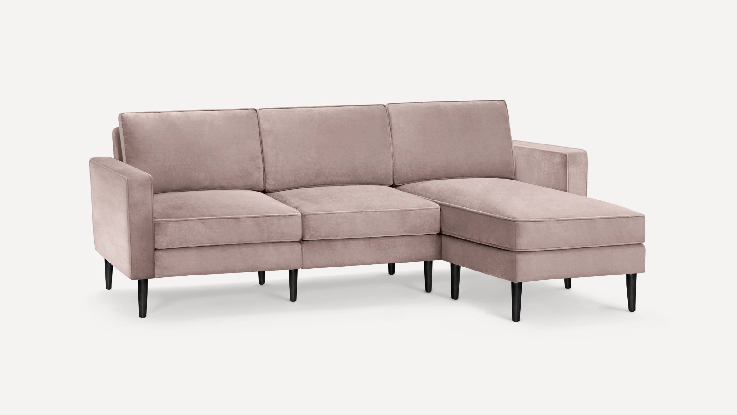 Blush pink velvet sectional sofa with three seat cushions, three back cushions, slim black legs, and a right chaise lounge.