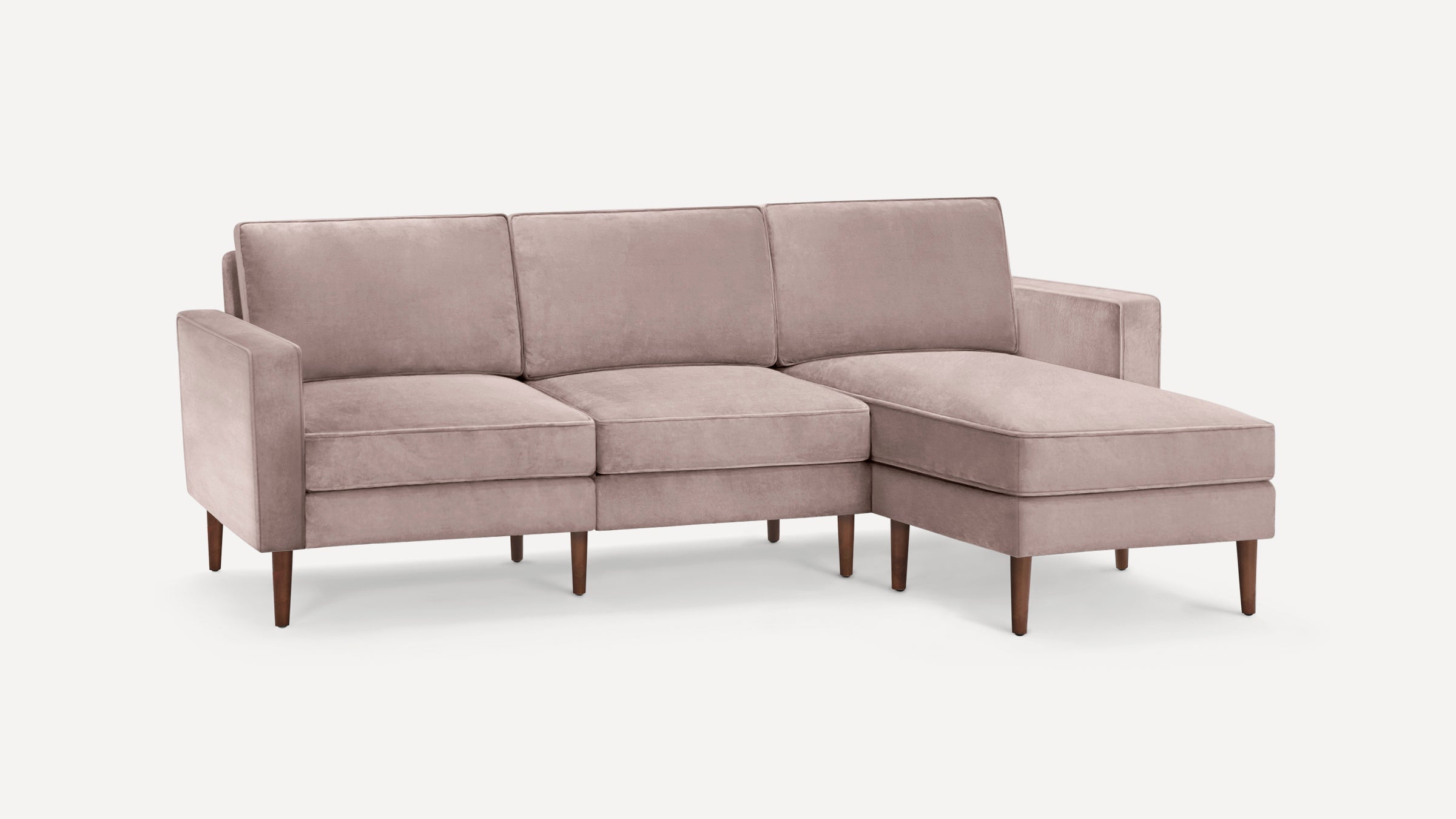 Modern blush pink velvet sectional sofa with wooden tapered legs and chaise lounge on the right side.