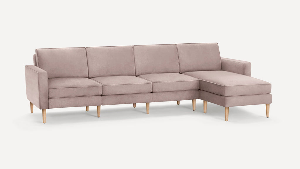 Modern light mauve sectional sofa with wooden legs, featuring four cushioned seats and a chaise lounge on the right side.