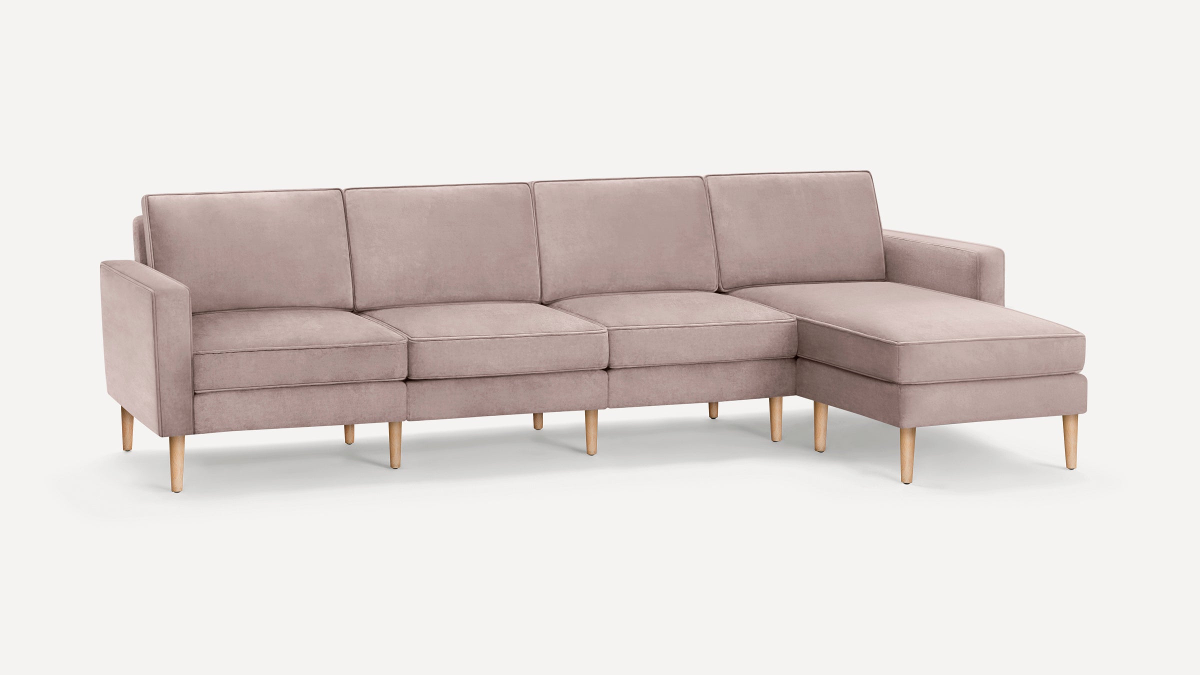 Modern light mauve sectional sofa with wooden legs, featuring four cushioned seats and a chaise lounge on the right side.