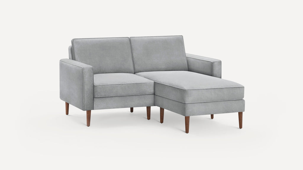 Light gray upholstered sectional sofa with right chaise, clean lines, and mid-century wooden legs on white background.