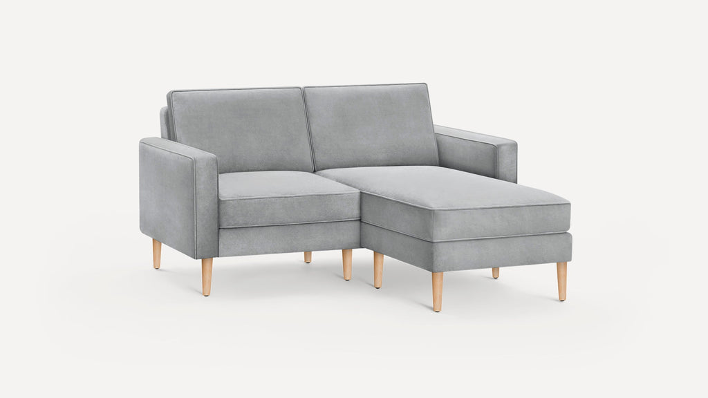 Light gray fabric sectional sofa with wooden legs and a chaise lounge on the right side, minimalist modern design.