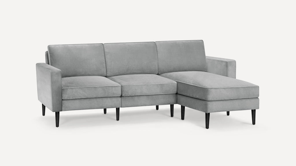 Modern light gray L-shaped sectional sofa with velvet upholstery, straight arms, cushioned seats, and slender black wooden legs.