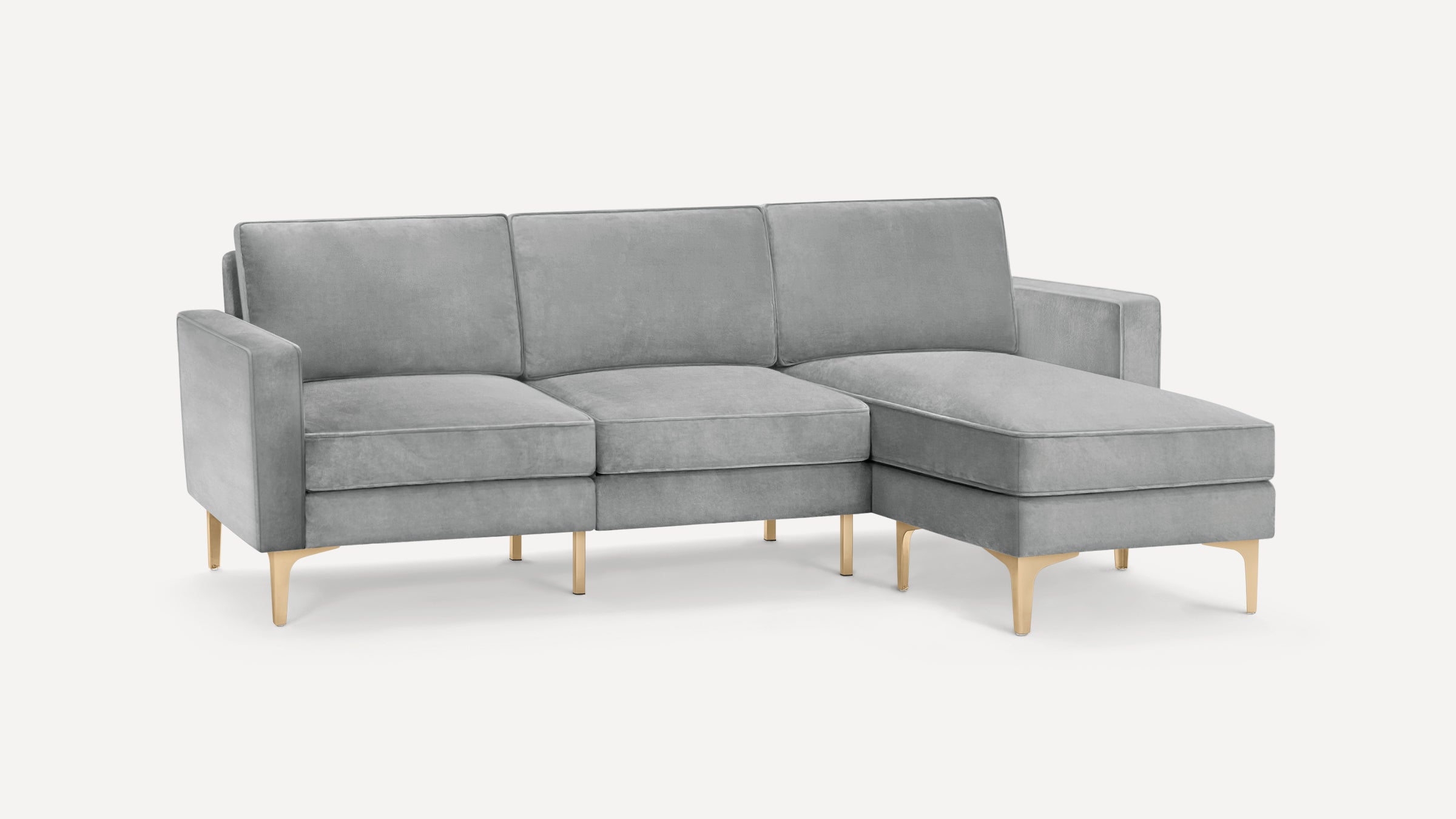 Light gray velvet L-shaped sectional sofa with gold metal legs and three back cushions on a white background.