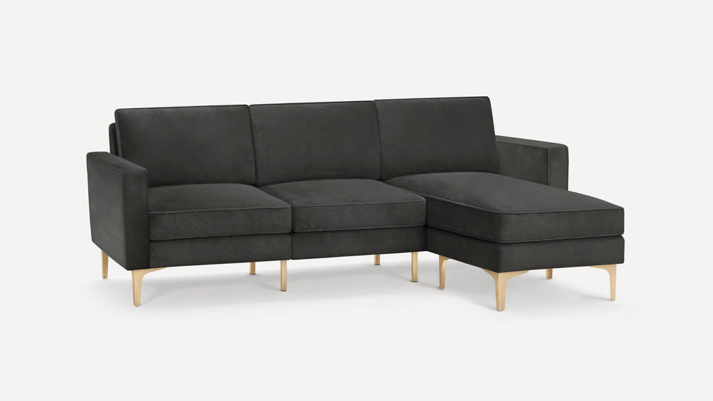 Dark gray sectional sofa with three seat cushions, a chaise on the right, square arms, and gold metal legs.