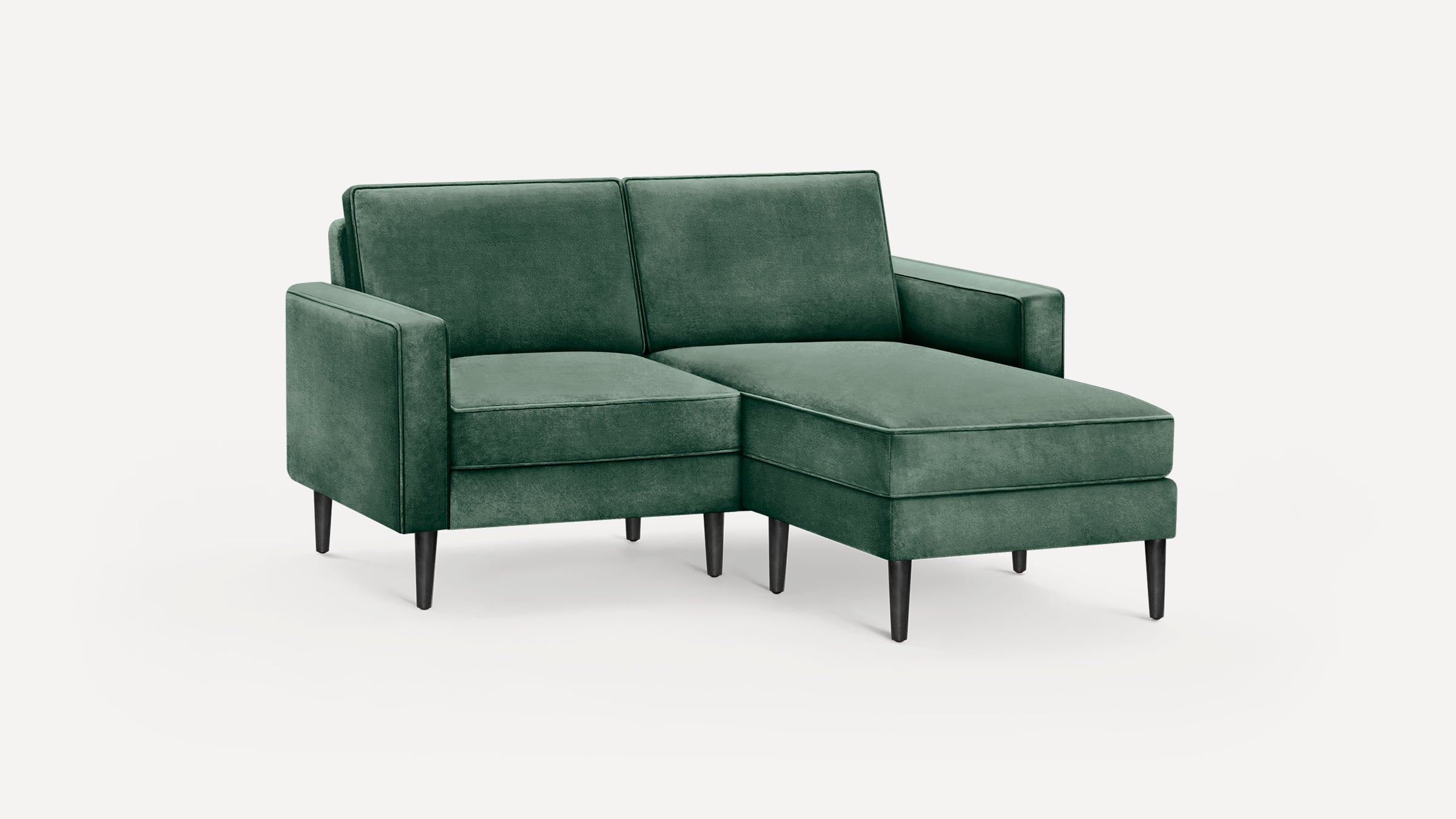 Modern green velvet sectional sofa with right chaise, square arms, and slender black wooden legs on white background.