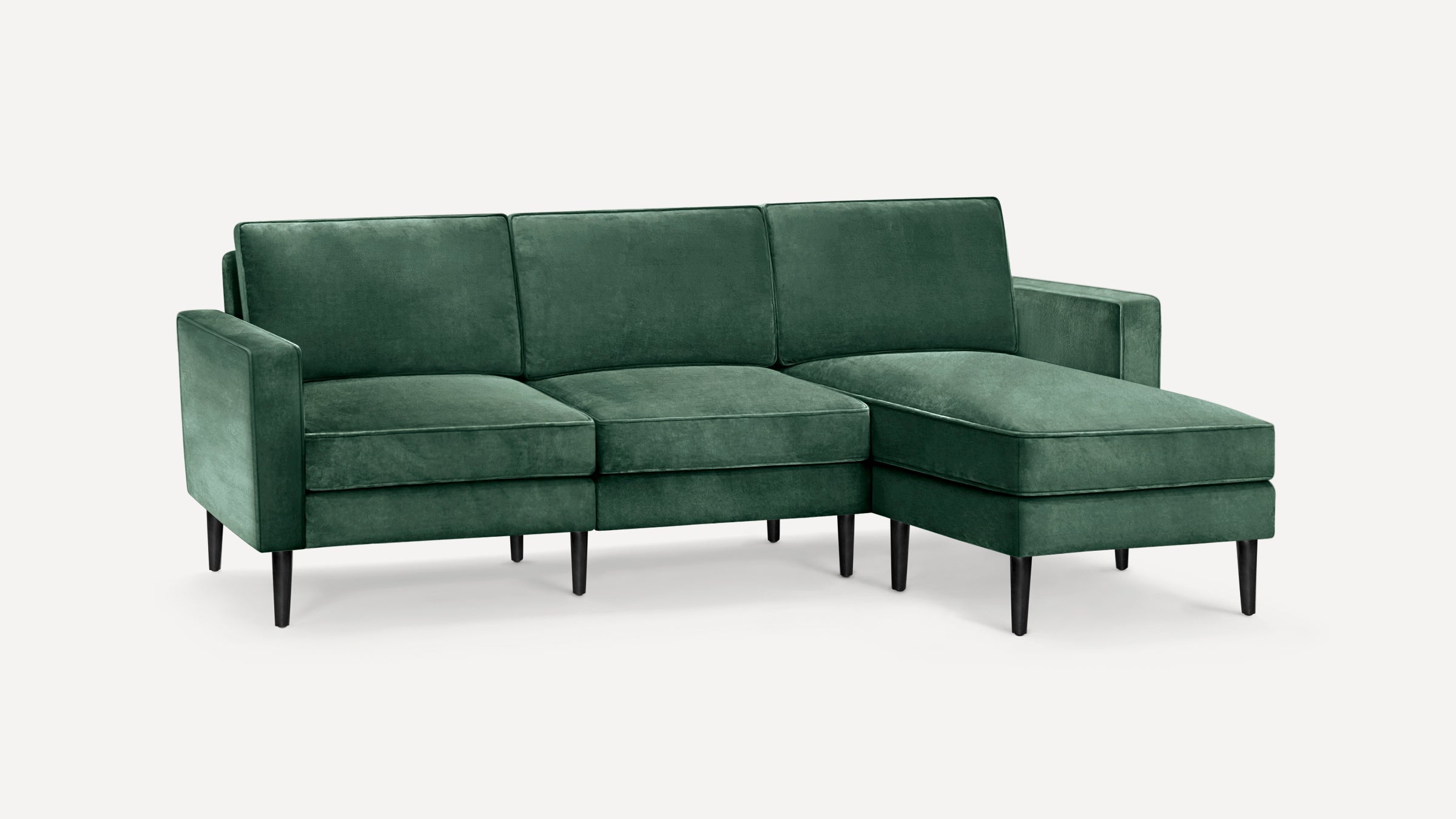 Modern green velvet sectional sofa with chaise lounge and black tapered wooden legs on white background.