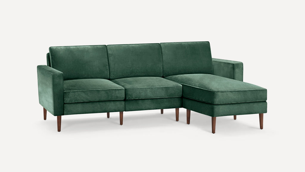 Dark green velvet L-shaped sectional sofa with wooden tapered legs and cushioned seats and backrests.