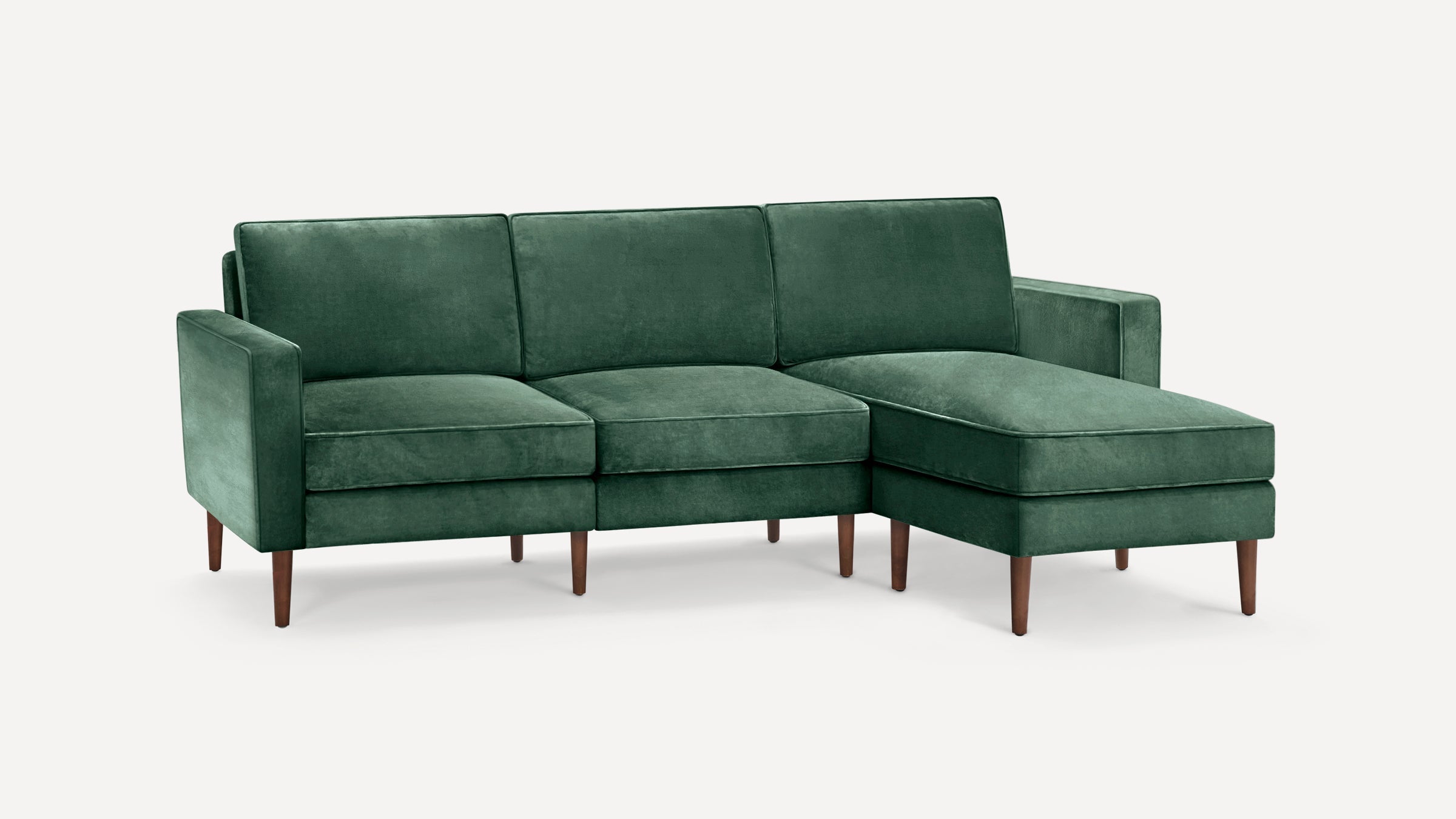 Dark green velvet L-shaped sectional sofa with wooden tapered legs and cushioned seats and backrests.