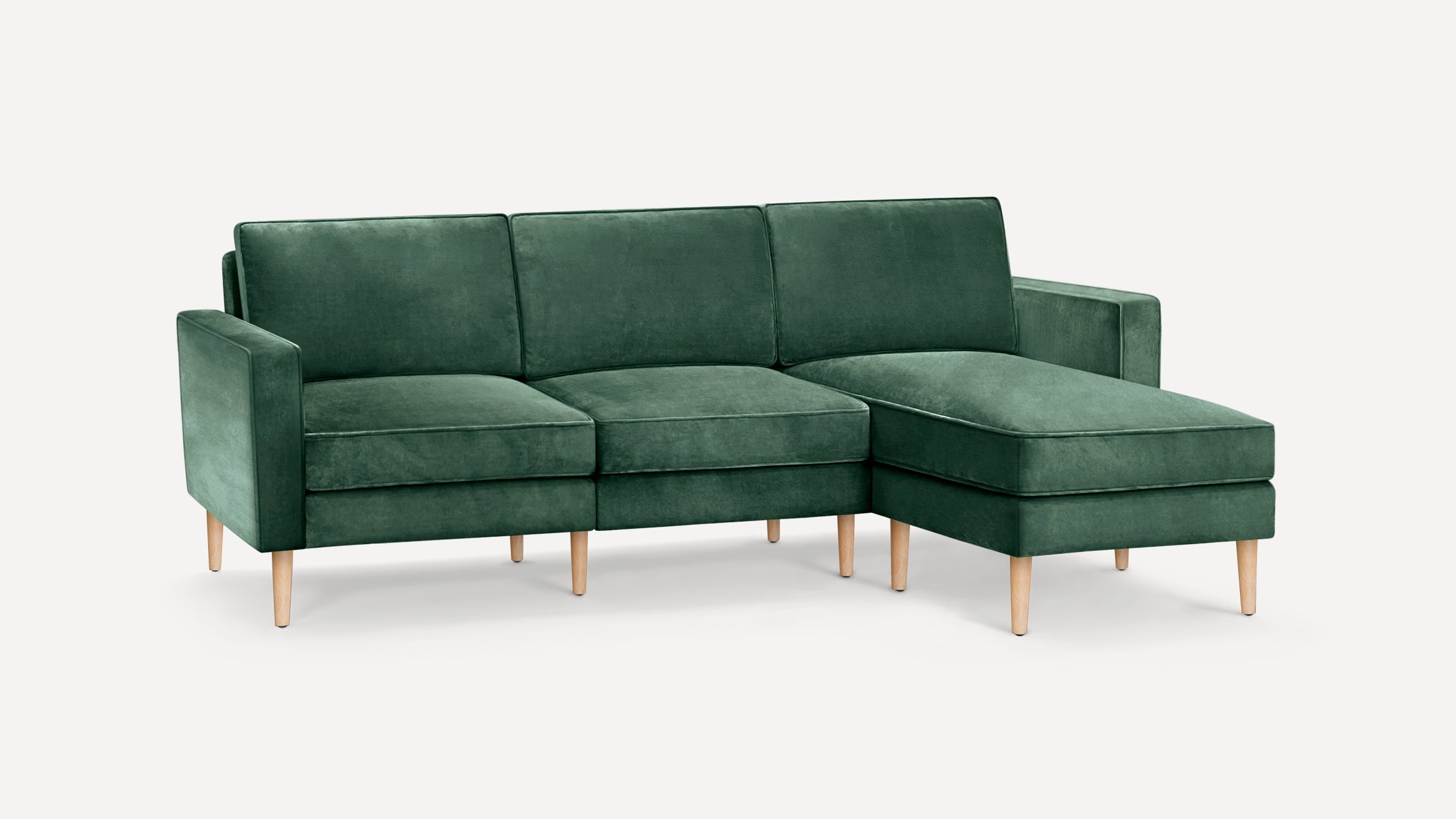 Green velvet sectional sofa with wooden tapered legs, including a chaise lounge on the right side, against a white background.