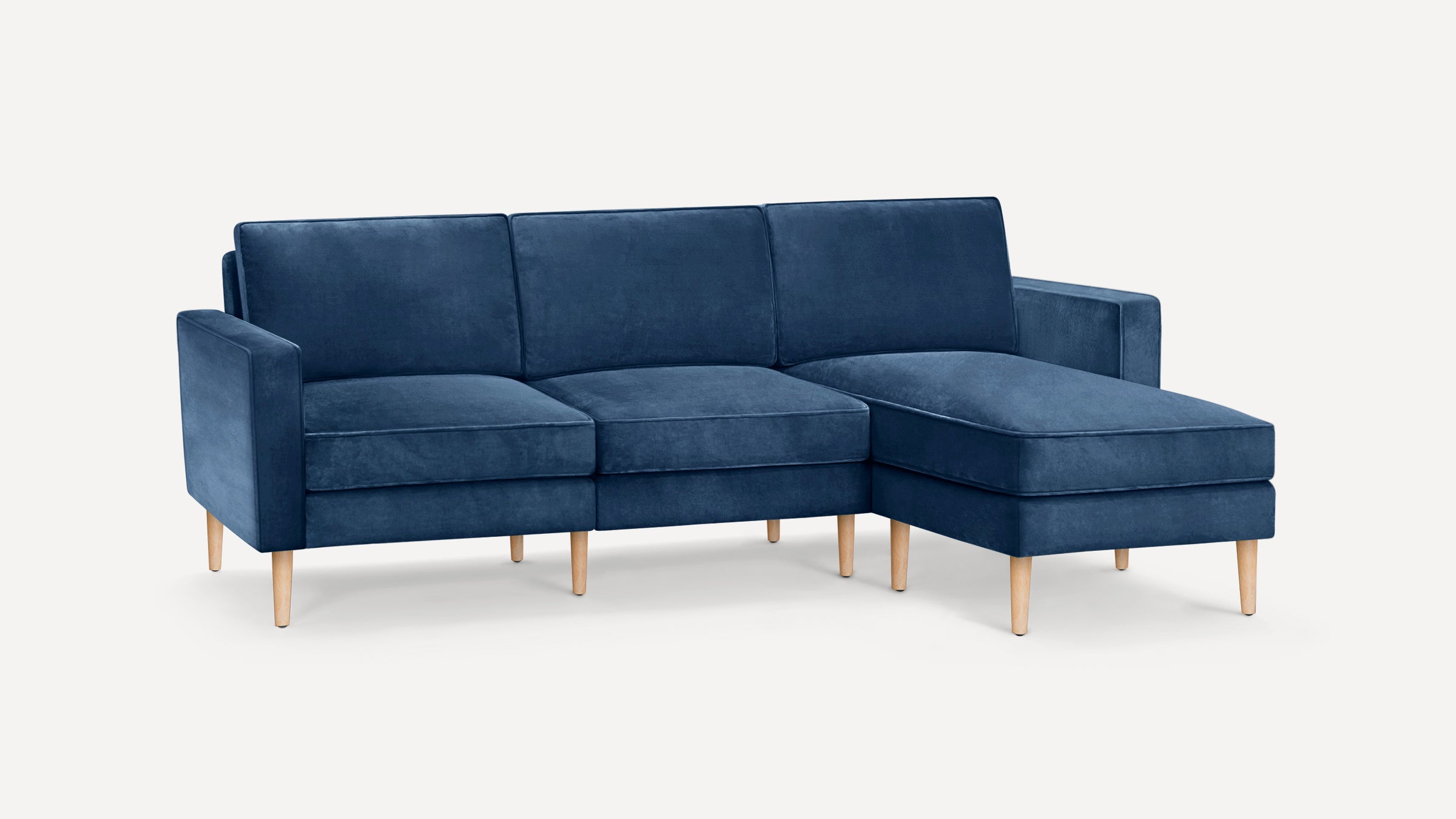 Modern navy blue velvet L-shaped sectional sofa with tufted cushions and light wooden legs on a white background.