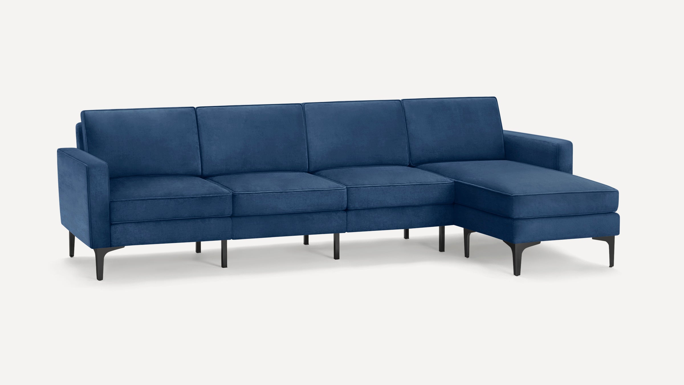 Modern sectional sofa in deep blue velvet with right chaise, slim black metal legs, and clean lines.