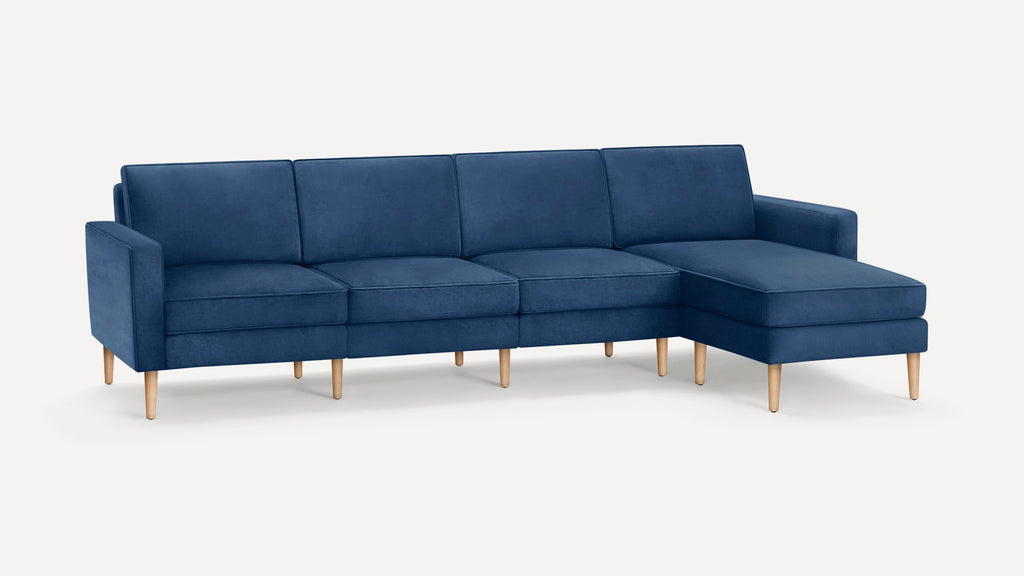 Modern sectional sofa upholstered in deep blue fabric with wooden legs and clean-lined cushions, including a chaise lounge on the right.