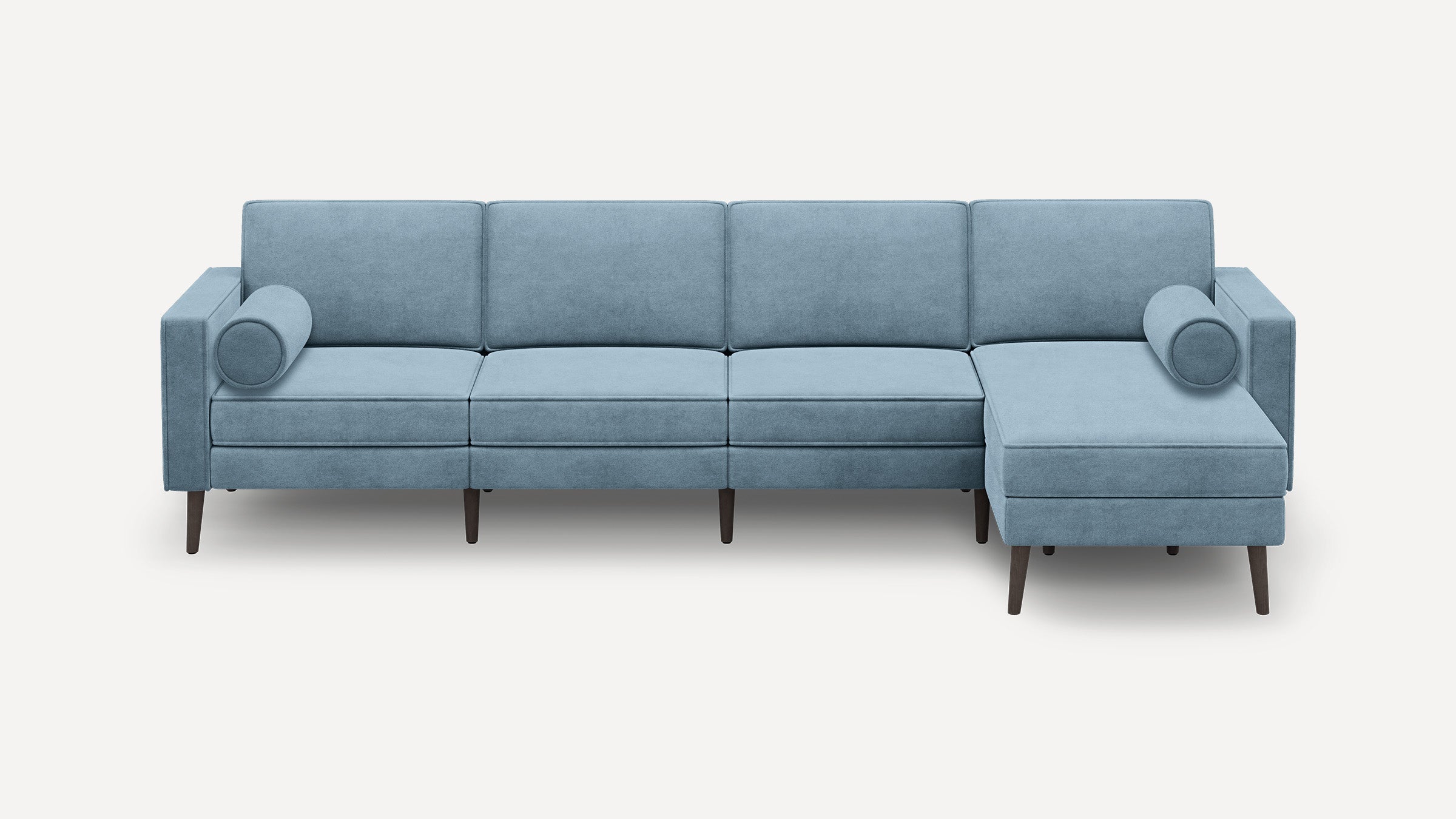 Modern light blue sectional sofa with chaise lounge, cylindrical pillows, and tapered wooden legs on white background.
