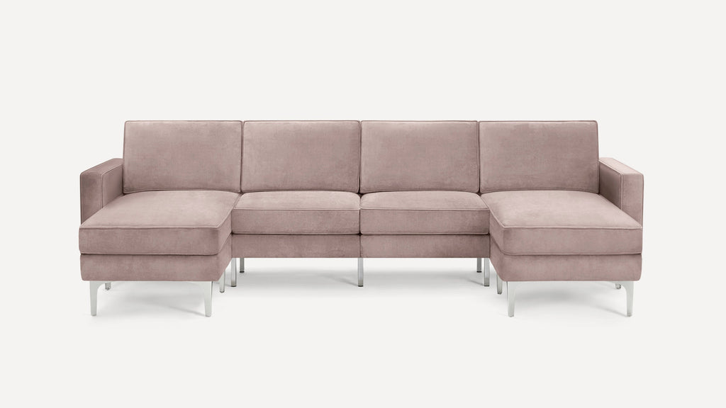 Modern U-shaped sectional sofa in soft blush pink fabric with cushioned seats and metal legs on white background.