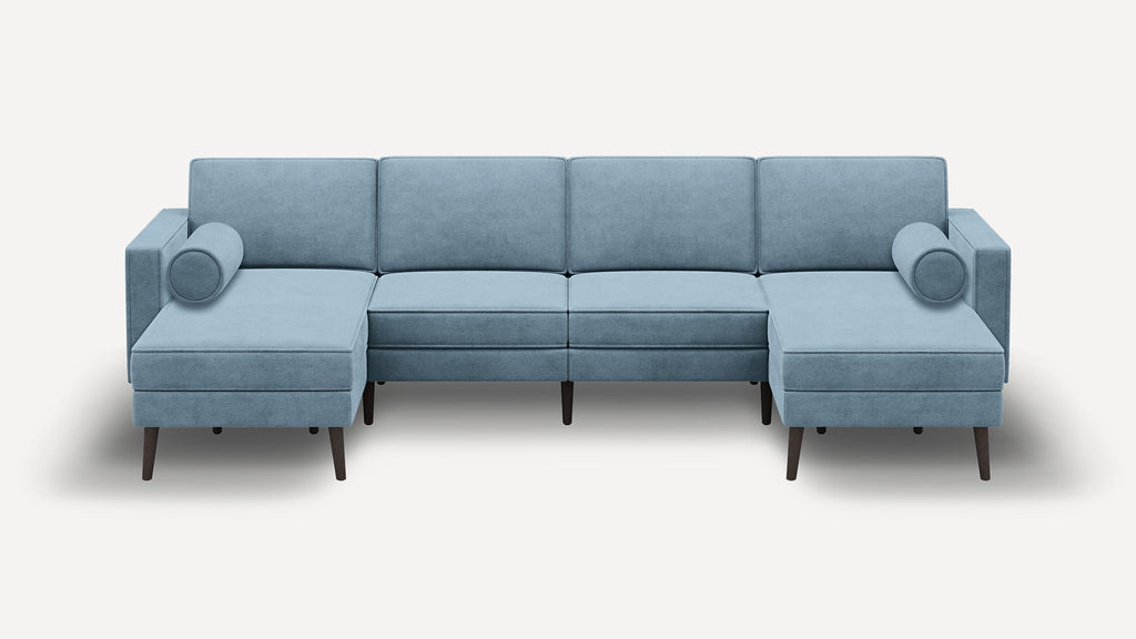 Modern light blue sectional sofa with clean lines, two cylindrical bolster pillows, and dark wooden legs on a white background.