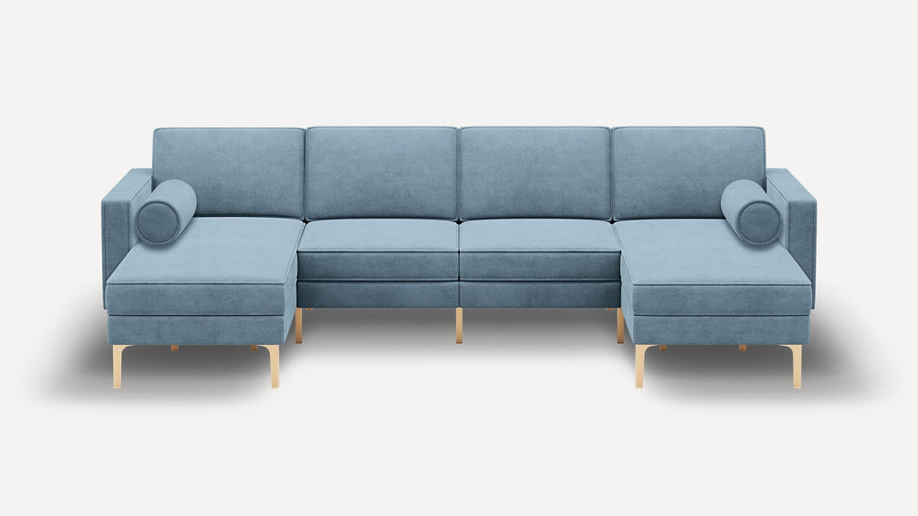 Modern sectional sofa in blue fabric with gold legs, featuring two chaise lounges and cylindrical bolster pillows on both ends.