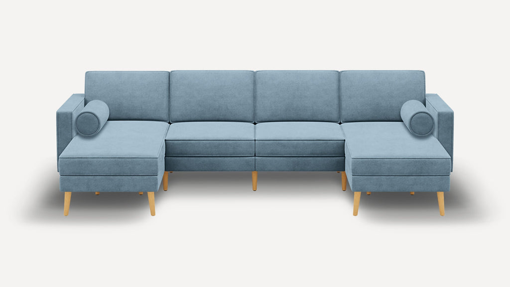 Modern light blue fabric sectional sofa with wooden legs, featuring chaise lounges on both ends and two cylindrical bolster pillows.