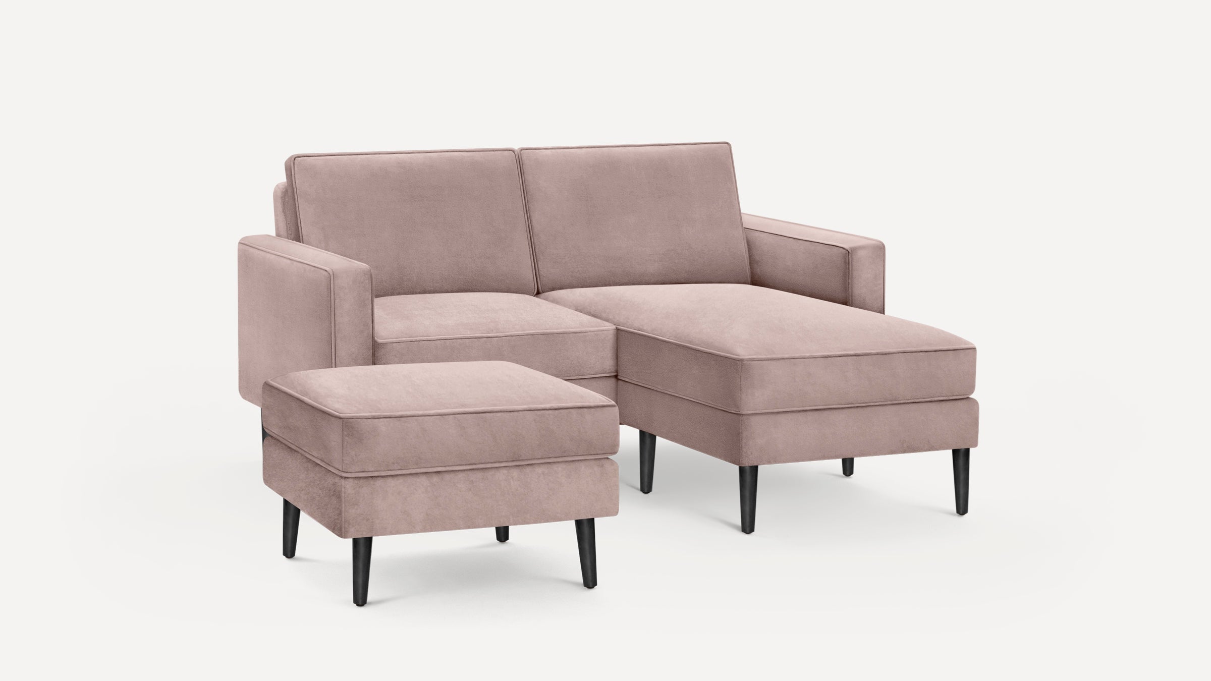 Modern blush pink sectional sofa with chaise lounge and matching ottoman, featuring black tapered legs and soft upholstery.