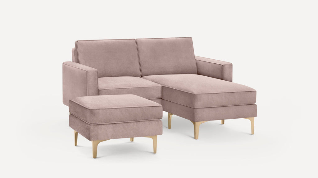 Modern dusty pink sectional sofa with matching ottoman, soft upholstery, gold metallic legs, and clean lines on a white background.