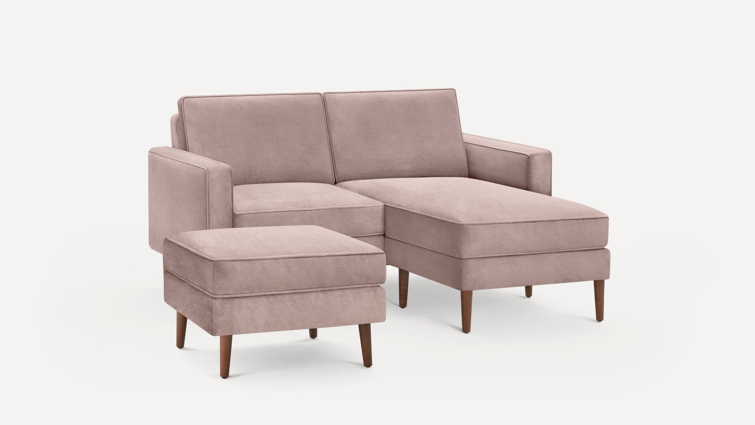 Light mauve velvet chaise sofa with matching ottoman, featuring clean lines and wooden tapered legs on white background.