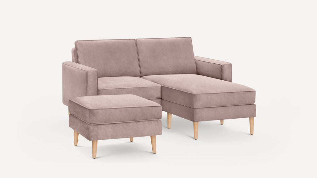 Modern mauve fabric sectional sofa with wooden legs, featuring a chaise lounge and matching ottoman.
